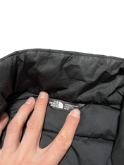 The North Face fekete női kabát belső címkéje, kézzel tartva, streetwear divat