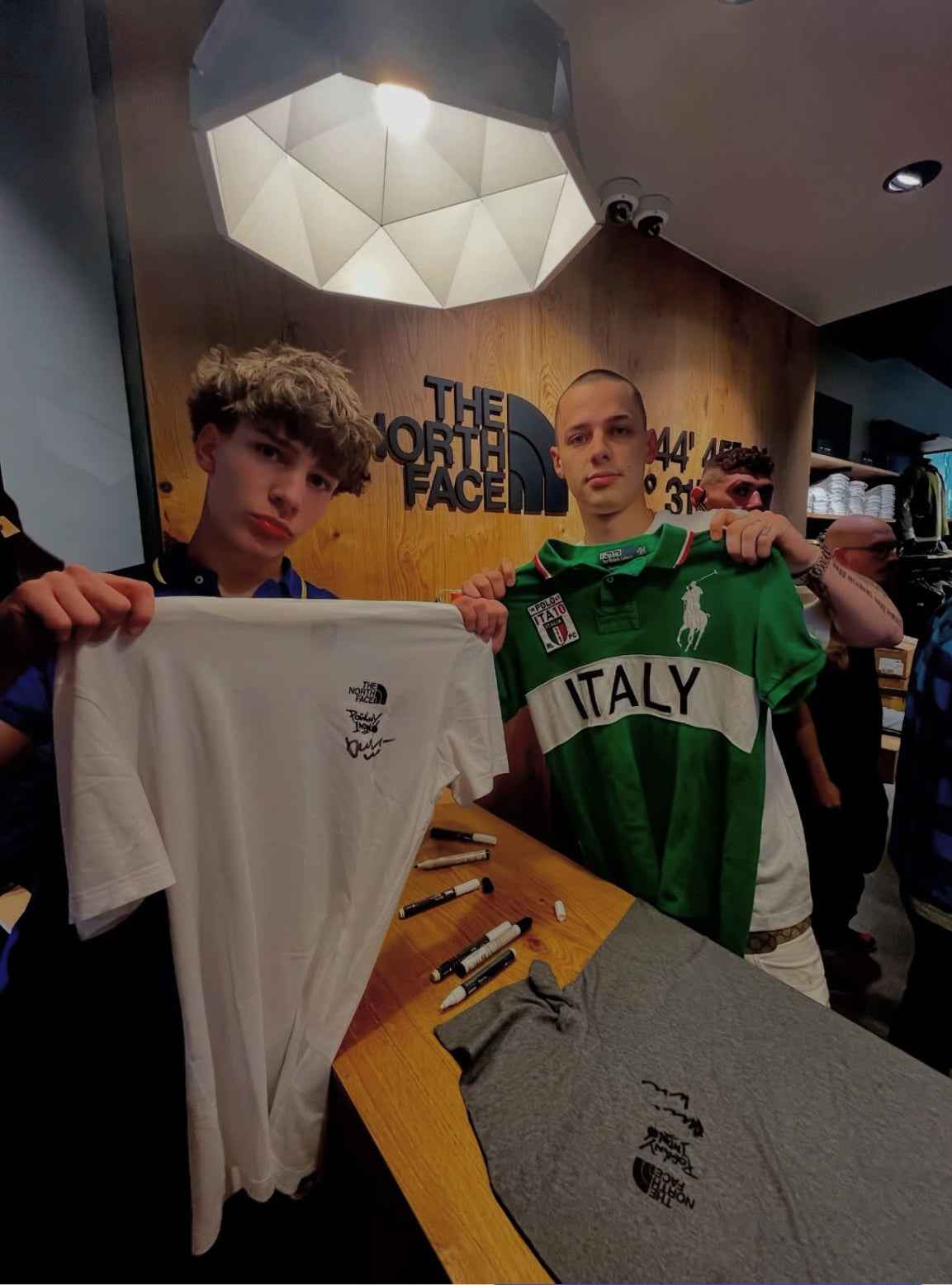 Fiatalok The North Face logós pólót és Ralph Lauren Italy pólót tartanak streetwear boltban