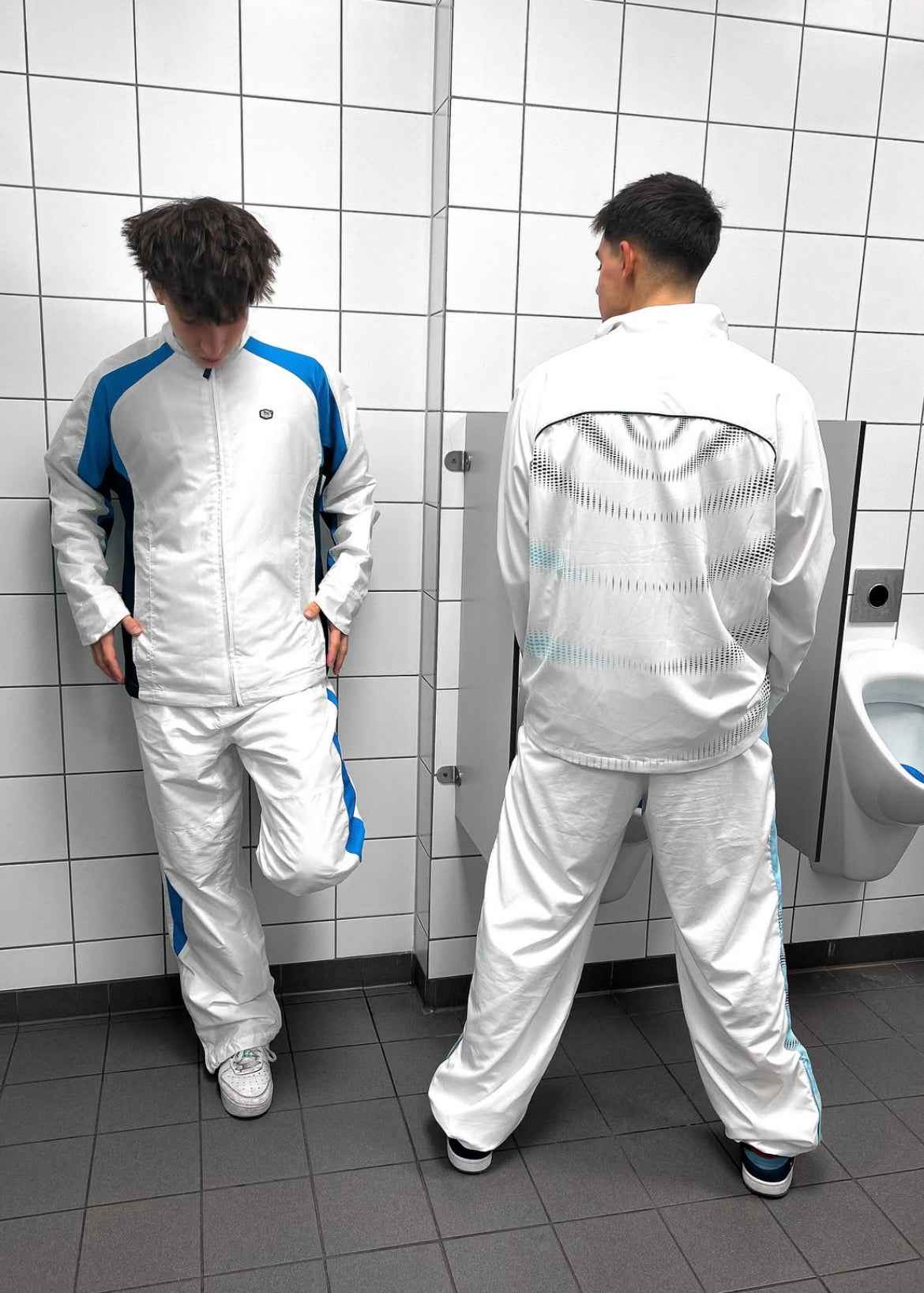 Két férfi fehér és kék vintage streetwear melegítő szettben, csempézett mosdóban.